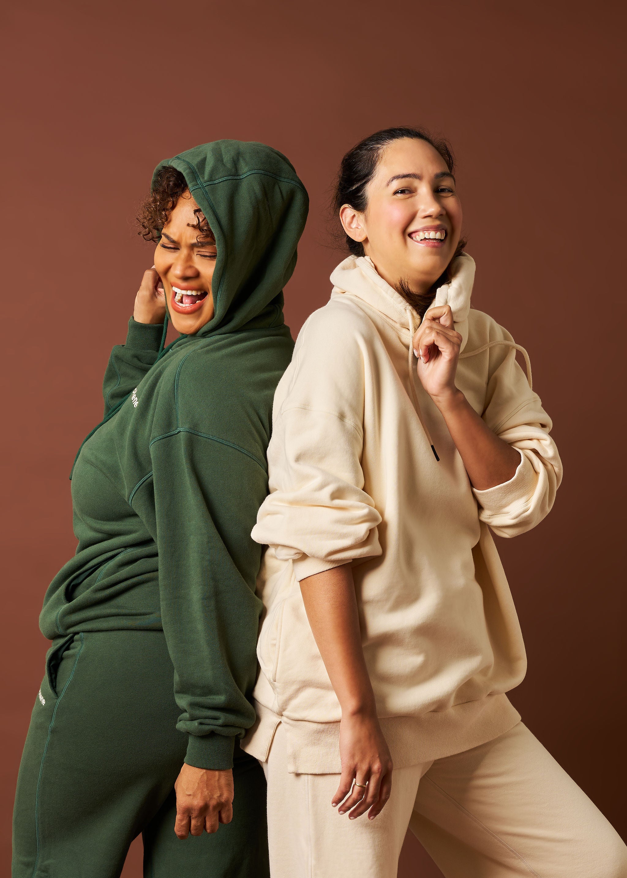Two women in Womene activewear, cream and coffee bean Workout Set, smiling on warm brown backdrop