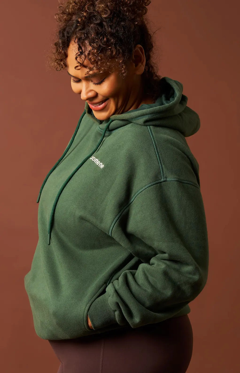 Person wearing a green hoodie with a logo on a brown background. Womene Australian women's cotton loungewear collection