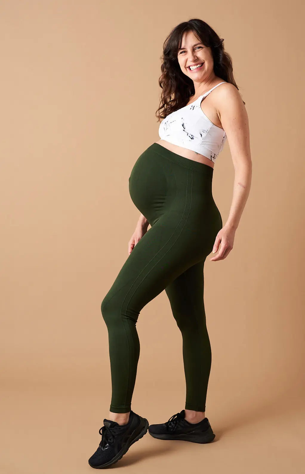 Woman wearing green leggings and a white sports bra on a beige background. Womene Australian maternity activewear collection