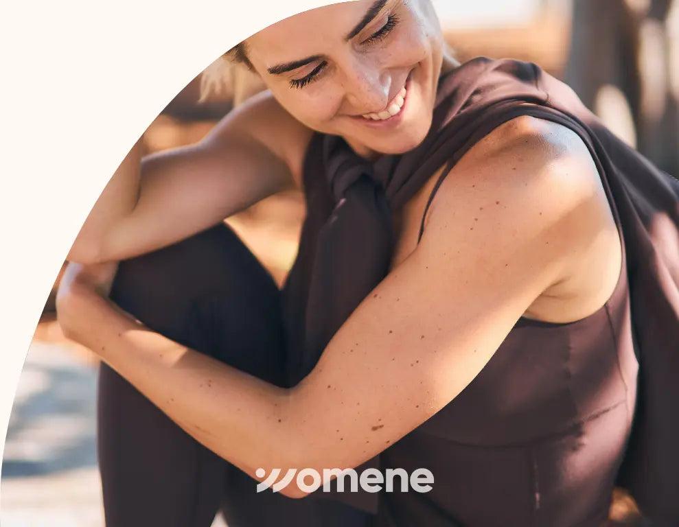 Woman wearing a dark brown dress with a blurred background, featuring the 'Womene' brand.Woman wearing Womene Moments activewear collection